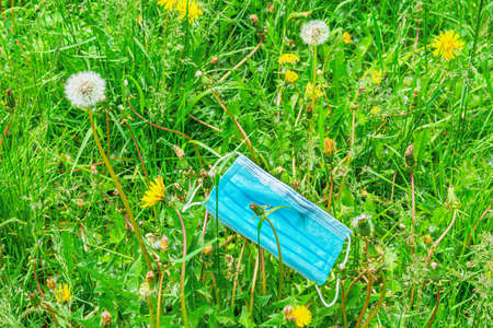 A medical mask is thrown in a dandelion field in the summer. Concept of wearing protective masks...