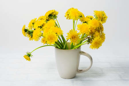 White mug with a bouquet of yellow dandelions on a white background. Table decoration. Isolated.の写真素材