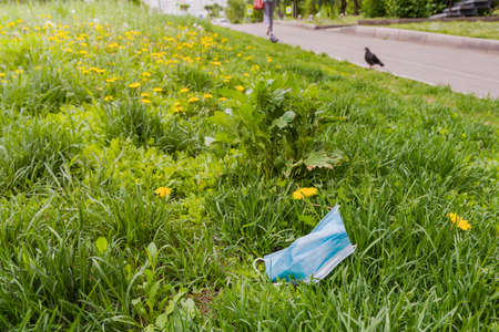 A used medical mask lies on the green grass in the city. A discarded protective mask.