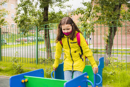 A 9-year-old schoolgirl girl in a yellow jacket is on the playground. Children go to school in September.の写真素材