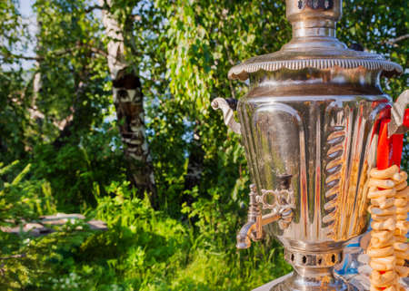 Summer tea in the open air. An antique samovar with bagels stands on a table in a birch forest.の写真素材