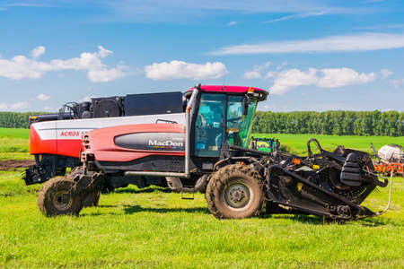 Krasnoyarsk, Russia - July 2, 2021: Canadian MacDon tractor with a mower on an agricultural field.