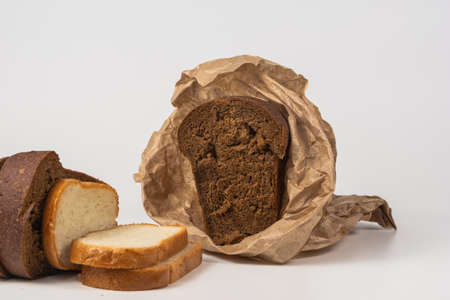 Slices of rye and wheat bread are laid out on a white background. Wrap half a loaf of dark bread in brown paper. Isolated.の写真素材