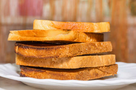 Several toasted slices of white bread are prepared for breakfast. Crispy toast is spread on a plate
