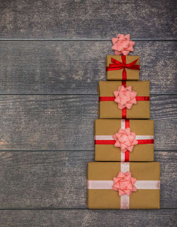 Four holiday gifts stacked in the form of a Christmas tree on a brown wooden background. New Year...