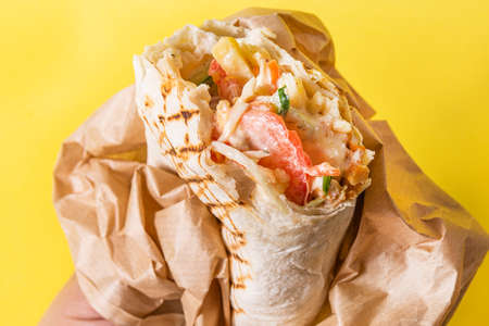 Shawarma slice in brown paper on a yellow background. Fast food.の写真素材