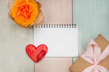 Rose, heart, notebook with a blank sheet and a gift on a colored wooden background. Flat lay.の写真素材