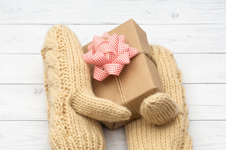 A holiday gift is enclosed in knitted woolen mittens. The concept of congratulations on the holidays that are in winter: Christmas, Valentine's Day, Birthday.の写真素材