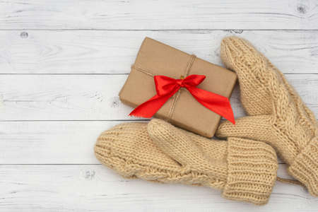 Knitted mittens hold a holiday gift on a white wooden background. The concept of congratulations to family and friends on the winter holidays.の写真素材