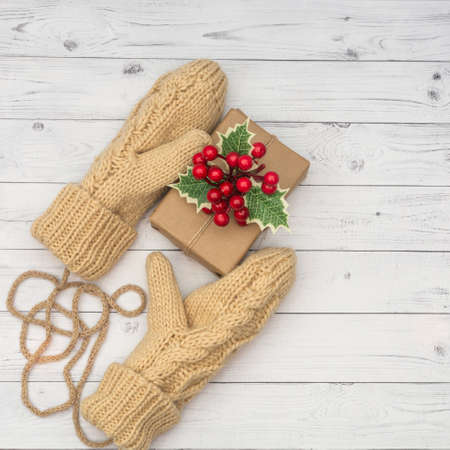 Knitted mittens hold a holiday gift on a white wooden background. The concept of congratulations to family and friends on the winter holidays.の写真素材