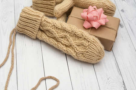 Knitted mittens hold a holiday gift on a white wooden background. The concept of congratulations to family and friends on the winter holidays.の写真素材