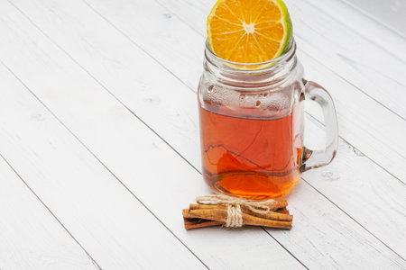 Black tea in a glass jar, lemon, cinnamon on a white wooden background. Copy space.