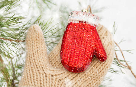 A hand in a thick knitted mitten holds a Christmas tree toy outdoors in winter. Christmas and New Year concept.の写真素材