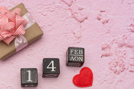 A gift, a heart and a calendar made of cubes with the date of February 14 are placed on a pink...