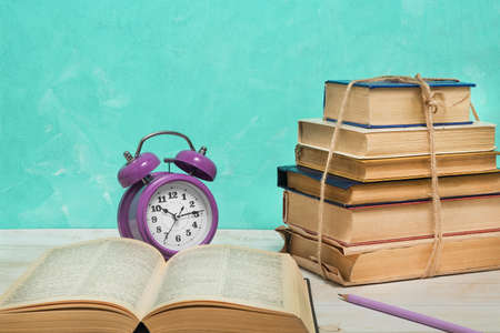 Alarm clock, open book and vintage books tied with twine. Education and wisdom conceptの写真素材