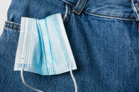A used medical mask sticks out of the front pocket of the jeans. Coronavirus concept