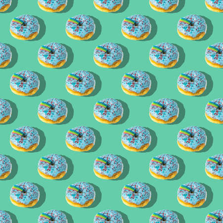 A repeating pattern of blue donuts with a rainbow on a green background. flat lay.の写真素材