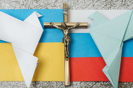On a gray background, a holy crucifix, the flags of Russia and Ukraine, paper doves of peace - origami. Conflict between Russia and Ukraine. The concept of establishing peace through prayer.の写真素材