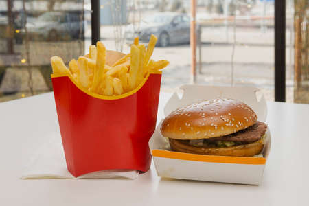 Sandwich with beef steak and fried french fries on a table in a cafe.