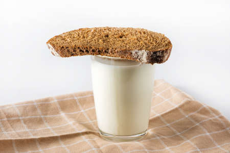 On a linen napkin stands a glass cup with milk and a slice of bread.