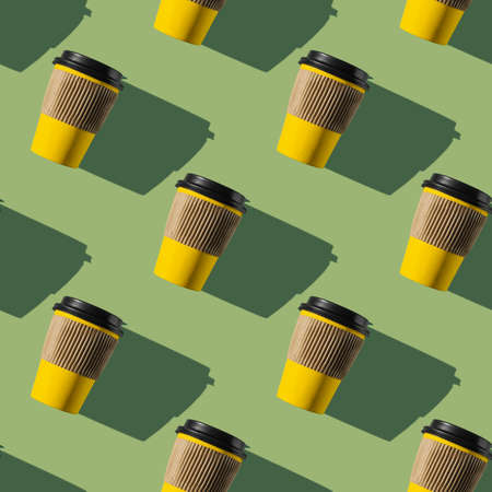 Pattern of yellow paper coffee cups on a green background. flat lay.