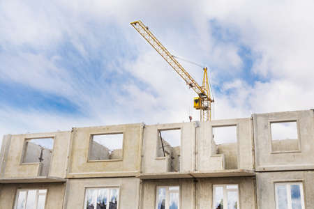 A large tower crane builds a house against a blue sky with clouds. Construction of an apartment...