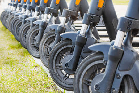 Ten scooters lined up in a summer parking lot. The image shows only the front wheels of the...
