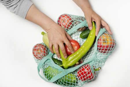 A woman puts vegetables and fruits in a reusable blue mesh bag. Cotton shopping bag - zero waste.