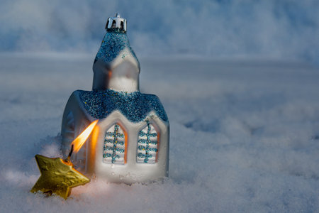 Festive decoration in the snow: a toy house and a burning candle in the form of a star. New Year and Christmas concept.の写真素材