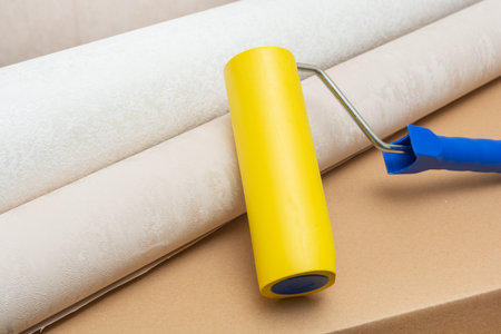Two rolls of wallpaper, a yellow roller lie on a brown cardboard box. The concept of renovation in a house or apartment.の写真素材