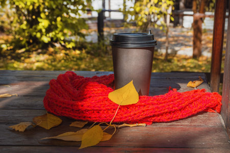 Autumn, a cup of coffee in a paper cup, a scarf and yellow leaves on a wooden table in an outdoor cafe. autumn concept.の写真素材