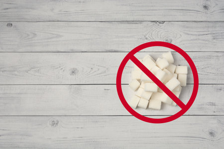 A pile of refined sugar and a red ring with a slash on a wooden background. The concept of giving up...
