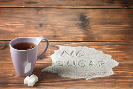 A purple cup with tea and a pile of sugar with the words - no sugar- are located on a brown background. The concept of reducing sugar intake to avoid illness.の写真素材