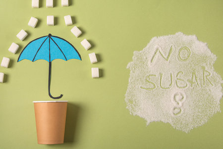 A paper cup is covered with an umbrella from sugar rain on a green background. The concept of...