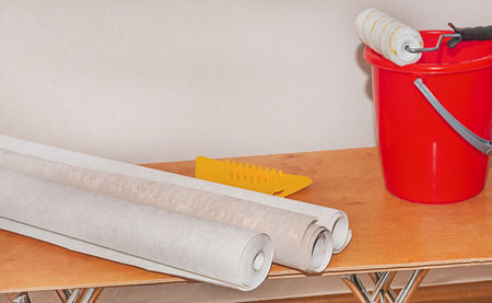Textured pastel wallpaper, a red bucket of glue and a roller are ready for a home renovation.の写真素材