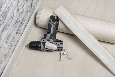 On the floor is a roll of linoleum, a baseboard and an electric screwdriver. Construction materials and a set of tools for laying linoleum. The concept of covering the floor with linoleum.の写真素材