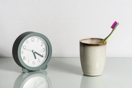 Alarm clock, toothbrush with pink bristles on glass surface of dressing table. Healthy teeth. Morning toilet concept.の写真素材