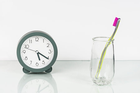 Alarm clock, toothbrush with pink bristles on glass surface of dressing table. Healthy teeth....