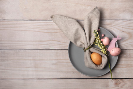 On the table there is a gray plate and a painted egg decorated with a bunny shaped napkin. Christian Easter tradition. Copy space. Flat lay.の写真素材