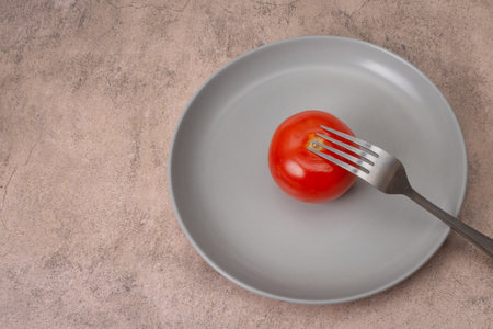 Red tomato lies on a gray plate, a fork is nearby. Flat lay.の写真素材
