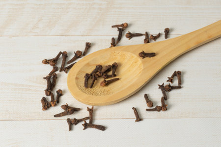 Dried cloves in wooden spoon on wooden light brown background. Top view. Flat lay.の写真素材
