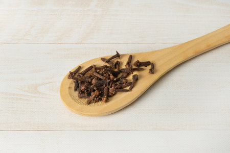 Dried cloves in wooden spoon on wooden light brown background. Flat lay. Top view.の写真素材