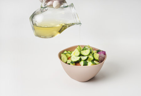 Mixed vegetable salad in a bowl on a white background. A woman's hand poured olive oil on the salad.の写真素材