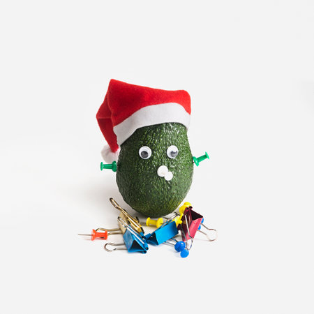 A cheerful little man made of green avocado in a Santa Claus hat with stationery instead of eyes and nose. Christmas and New Year in the office, Creative design ideas.の写真素材