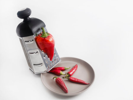 One large red bell pepper is grated to produce a bunch of small red chili peppers, which are placed...