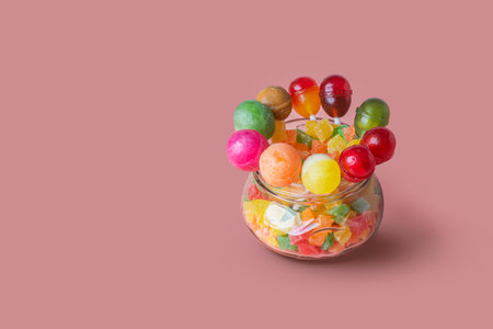 A group of multicolored lollipops in a glass jar on a pink background. Copy space.の写真素材