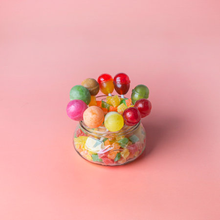 A group of multicolored lollipops in a glass jar on a pink background. Copy space.の写真素材