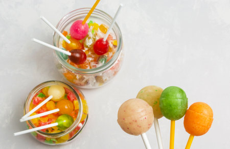 Four spherical lollipops against a background of jars of multi-colored lollipops. Top view.