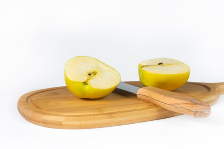 An apple is being sliced with a knife on a wooden cutting board. White background. Isolated.の写真素材