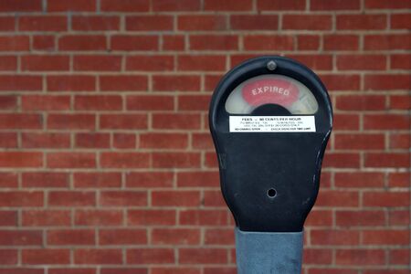 An expired parking meter with brick wall background.の写真素材